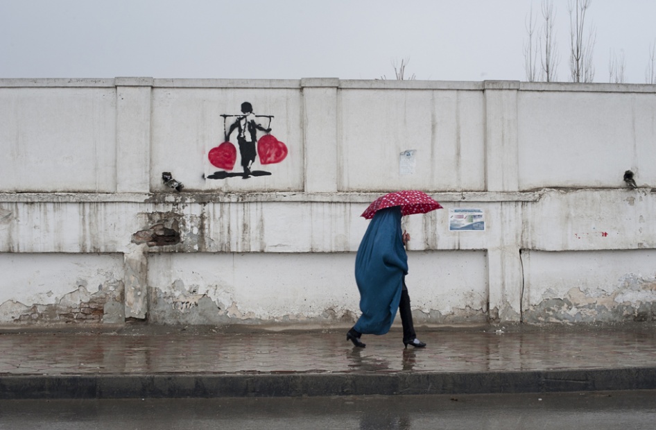 Kabul is a place to be. 
A woman walking in one of the main street of Kabul. On the wall, Banksys anti-war project.
Kabul is a place to be. Anything  is possible because everything has to be rebuilt. The city attracts high level war specialists as well as fabulous artists.
